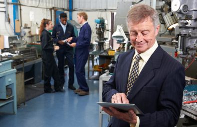Owner Of Engineering Factory Using Digital Tablet With Staff In Owner Of Engineering Factory Using Digital Tablet With Staff In Background