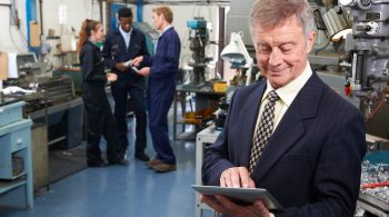 Owner Of Engineering Factory Using Digital Tablet With Staff In Background