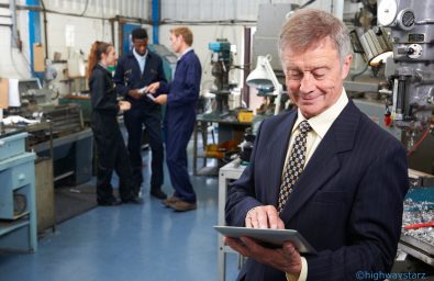 Owner Of Engineering Factory Using Digital Tablet With Staff In Background