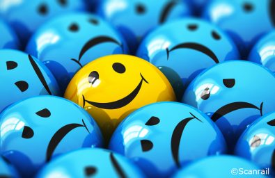 Creative abstract success and people emotion concept: macro view of happy yellow smiley face ball icon or button among dull sad blue ones with selective focus effect